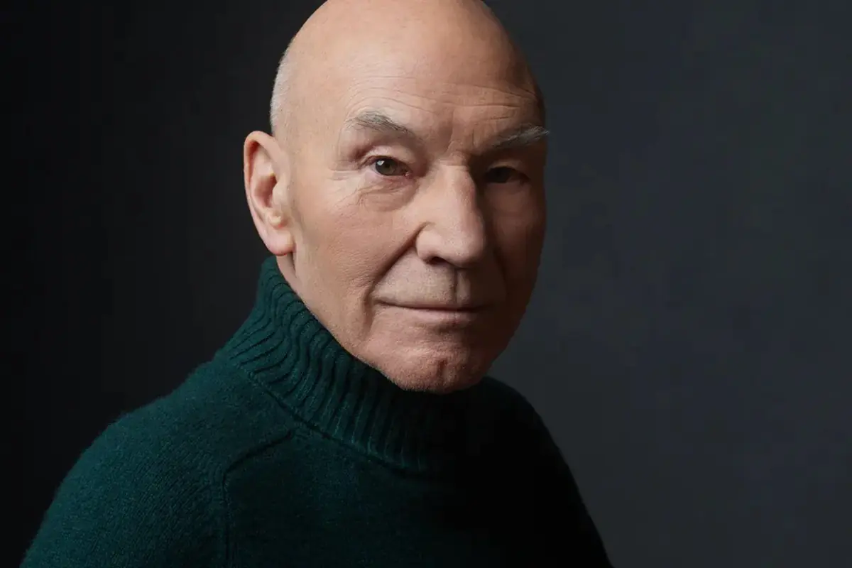 Sir Patrick Stewart - THEWILL NEWS MEDIA Portrait of an older, bald man wearing a dark green turtleneck against a dark gray background.