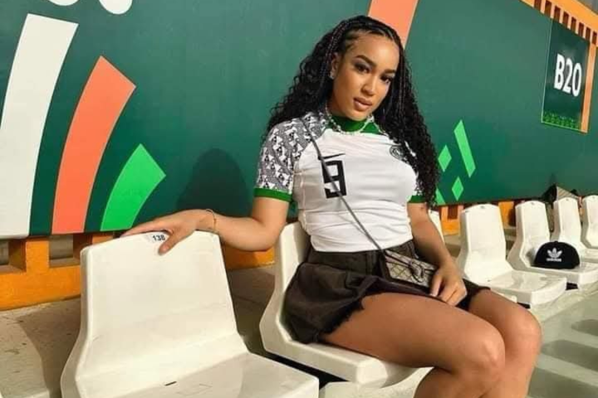 Stephanie Ladewig - THEWILL NEWS MEDIA Young woman with braided hair wearing a white-green top and black shorts sits on white stadium seats beside a green mural.
