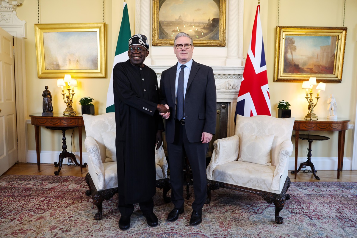 Tinubu - THEWILL NEWS MEDIA Two dignitaries shake hands in a formal room with Nigerian and UK flags behind them, seated between two ornate chairs and a fireplace.