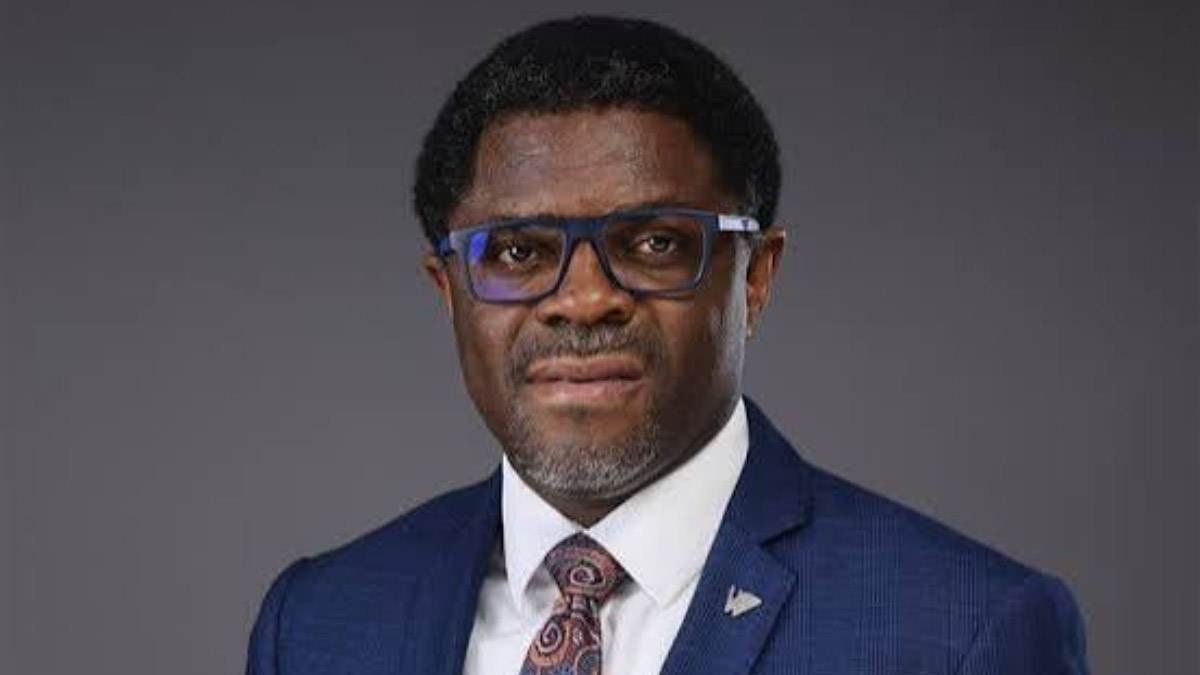 Tunde Mabawonku - THEWILL NEWS MEDIA Portrait of a man in a navy suit, white shirt, paisley tie, and blue glasses against a gray background.